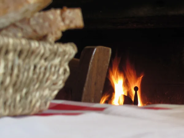 Палаючий камін з кошиком хліба і старовинним вінтажним стільцем в заміській атмосфері — стокове фото