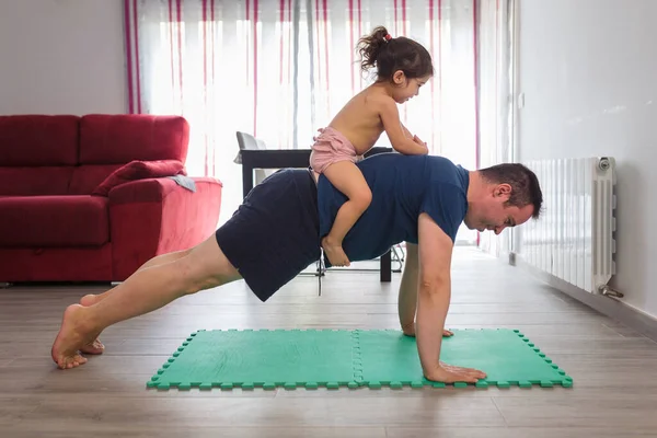 Caucasian father does sports, fitness and yoga with his baby girl of Latin mother in the dining room of the house, they have fun while they do the exercises.