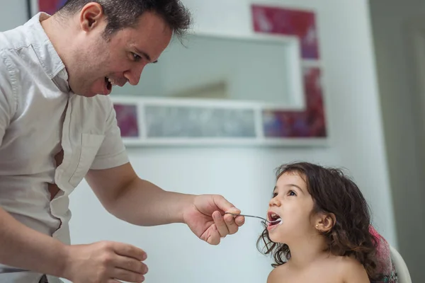 一位面带微笑 面带微笑的白人父亲把酸奶喂给了一位坐在家中高脚椅上的两岁小女孩 — 图库照片
