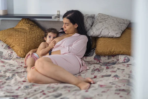라틴계 어머니는 분홍색 가운을 침대에서 딸에게 모유를 먹이고 — 스톡 사진