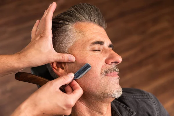 一个白人理发师的手正要在理发店里用一把经典的剃须刀刮胡子 — 图库照片
