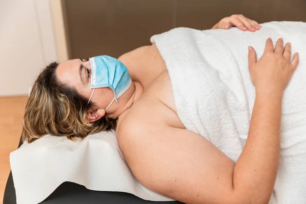 Una mujer está acostada sobre una máscara de prevención del coronavirus esperando una terapia física — Foto de Stock