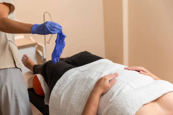 Physiotherapist puts latex gloves next to patient — Stock Photo, Image