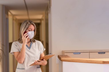 Hemşire hastanede elinde bir dosya ve koruyucu maskeyle telefona cevap veriyor.