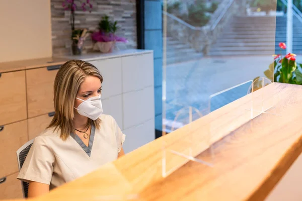 Receptionist dal centro di fisioterapia dietro la scrivania con maschera pandemica — Foto Stock