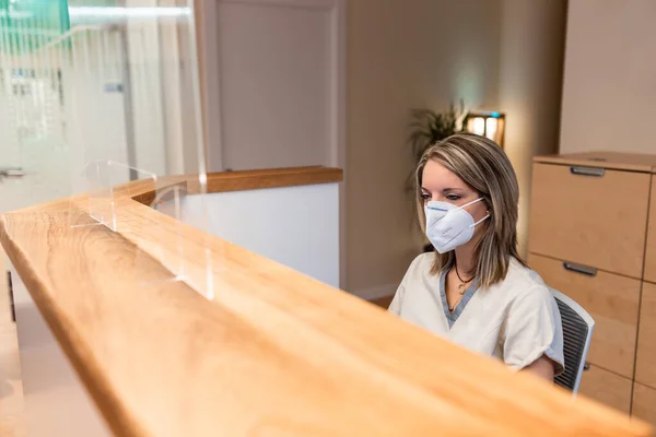 Receptionist dal centro di fisioterapia dietro la scrivania con maschera pandemica — Foto Stock