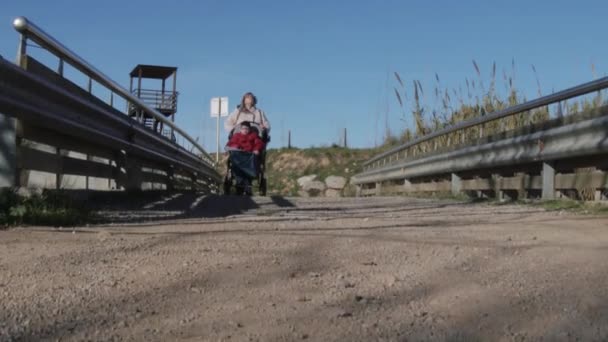 Donna sedia a rotelle passaggio bambino disabile su una strada sterrata. — Video Stock