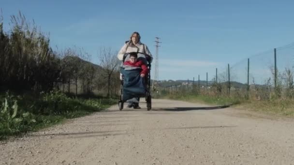 Nő kerekesszékes pass fogyatékkal élő gyermek a földúton. — Stock videók