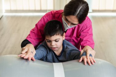 Fıstık Beden Eğitimi Balosu 'nda denge egzersizleri yapan engelli bir çocuk ve fizyoterapist. salgın maskesi koruması