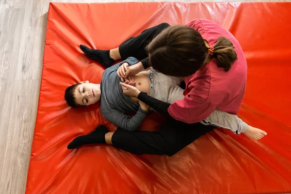 Postižené dítě a fyzioterapeut na červené gymnastické podložce dělat cvičení. ochrana pandemické masky — Stock fotografie