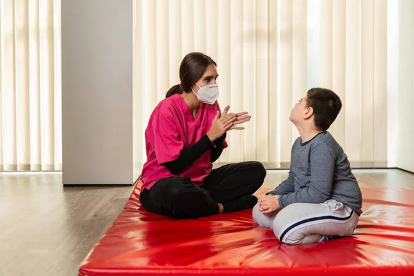 Инвалид ребенок и физиотерапевт на красном гимнастическом коврике делает упражнения. пандемическая защита маски — стоковое фото