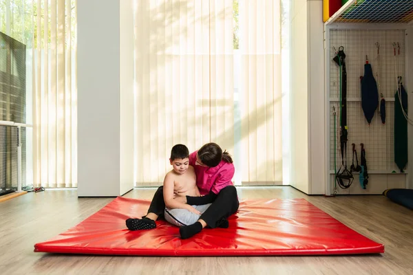 Enfant handicapé et physiothérapeute sur un tapis de gymnastique rouge faisant des exercices. protection masque pandémique — Photo