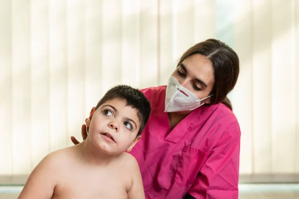 Behindertes Kind und Physiotherapeut auf einer roten Gymnastikmatte bei Übungen. Pandemieschutz — Stockfoto