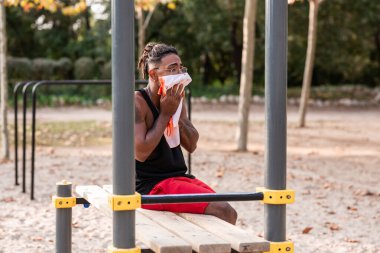 Afro-Amerikalı sporcu çocuk, parkta spor yaptıktan sonra dinleniyor ve havluları çıkartıyor.