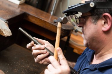 Bir kuyumcu gümüş bir yüzük tutar ve onu küf ve çekiçle şekillendirir..