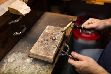 Kuyumcu tezgahta lehimlenmiş gümüş bir yüzük lehimliyor..