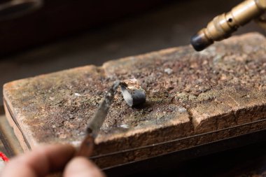 Kuyumcu tezgahta lehimlenmiş gümüş bir yüzük lehimliyor..