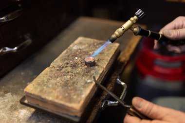 Kuyumcu tezgahta lehimlenmiş gümüş bir yüzük lehimliyor..