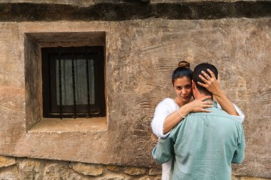 Eski bir evin duvarında kucaklaşan bir çift. Kız şehvetli bir şekilde bakıyor..