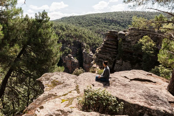 Ein Mädchen sitzt auf dem Felsen einer Klippe, bergige Landschaft mit Wald — Stockfoto