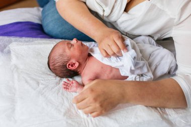 Anne yeni doğmuş oğluna yumuşak, beyaz bir beden giydirip değişen bir minder giydirip hassas bir bağ ve bakım yaratıyor.