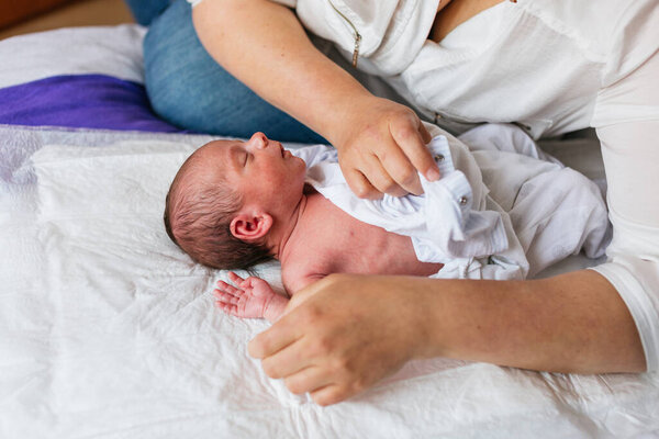 Mother gently dressing her newborn son in a soft white bodysuit on a changing mat, creating a moment of tender connection and care