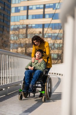 Önemseyen bir anne, şehirde bir köprüde gezinirken, engellilerle oğlunu teselli ediyor, destek ve sevgi sunuyor.