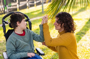 Parkta birlikte oynayıp, el ele tutuşup dışarıda kaliteli vakit geçirmenin keyfini çıkaran engelli bir anne ve oğul.