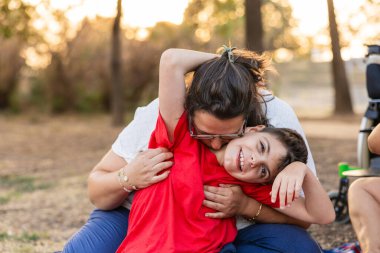 Anne sevgisini ve sevgisini, gülümseyen beyinsel felçli çocuğuna dışarıda sarılarak, gün batımında ailecek vakit geçirerek gösteriyor.