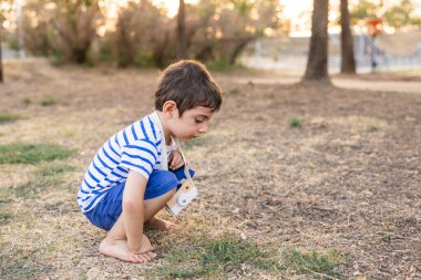 Küçük çocuk dışarıda oynuyor, çömelmiş, oyuncak kamerasıyla doğayı keşfediyor ve çocukluğunda hayal gücünü kullanıyor.