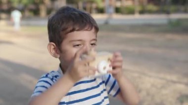 Serebral felçli bir çocuk parkta tahta bir oyuncak kamerayla oynuyor. Tatlı çocuk güneşli bir günün tadını çıkarıyor, fiziksel zorlukların üstesinden geliyor.