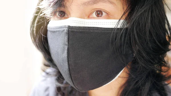 Close-up of person wearing double face masks by covering a disposable mask with a cloth face mask to increases protection against the coronavirus COVID-19 pandemic.
