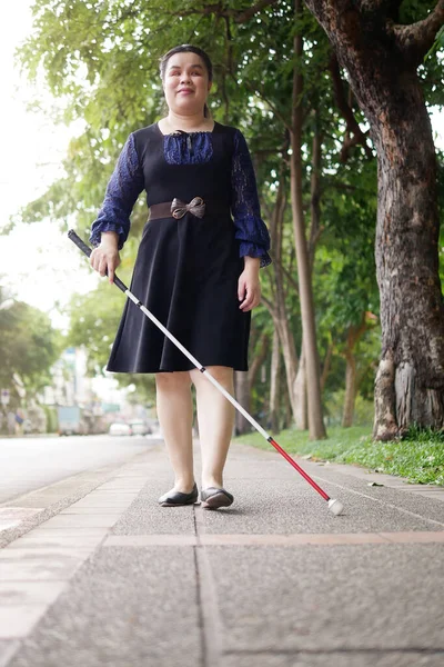 Asian blind person woman walking on sidewalk with a long white cane a mobility tool used to detect objects in the path, also helpful for onlookers in identifying the user as blind or vision disability