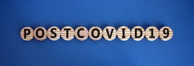 The word 'postcovid19' on wooden circles on beautiful blue background, copy space. Covid-19 pandemic and medical concept. clipart