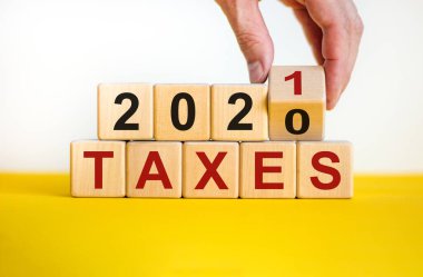 İş planı 2021. Erkek eli ahşap küpü çevirir ve 'Vergiler 2020' yazısını 'Vergiler 2021' olarak değiştirir. Güzel sarı masa, beyaz arkaplan, kopyalama alanı.