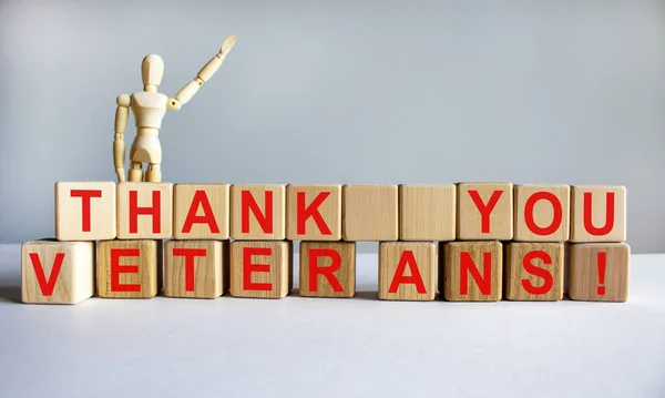 Concept words \'thank you veterans\' on cubes on a beautiful white table. Wooden model of human. White background. Concept, copy space.
