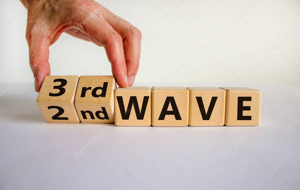 Symbol for a third wave of the corona virus. Hand turns a cube and changes the expression '2nd wave' to '3rd wave'. Copy space. Beautiful white background.