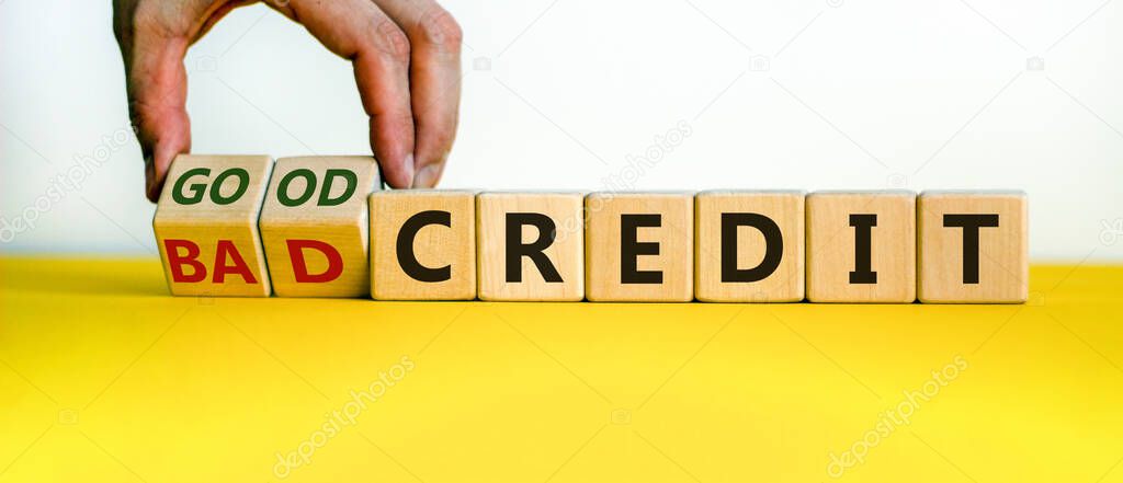 Male hand flips wooden cubes and changes the words 'bad credit' to 'good credit' or vice versa. Beautiful yellow table, white background, copy space. Business concept.