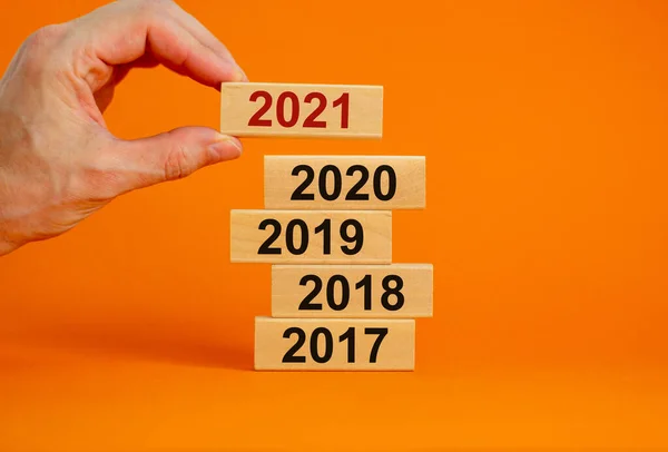 Male hand placing a block with number \'2021\' on a blocks tower with numbers \'2017, 2018, 2019, 2020\'. Beautiful orange background. Copy space. Business and new year concept.