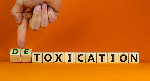 Hand flips cubes and changes the expression 'toxication' to 'detoxication'. Beautiful orange background. Healthy lifestyle concept. Copy space.