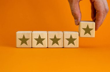 Güzel turuncu arka planda altın yıldız işaretli tahta küpleri, kopyalama uzayı. Erkek eli. Kalite ve lüks kavramsal imaj. Boşluğu kopyala.