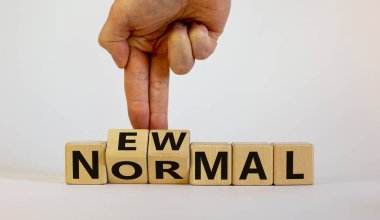 Yeni normal ve covid-19 salgını. Tahta küplerde, güzel ahşap bir masada 'yeni normal' kelimeler. Erkek eli. Güzel beyaz arka plan. Boşluğu kopyala.