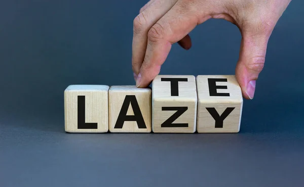Late and lazy. Male hand flips wooden cubes and changes the word \'lazy\' to \'late\' or vice versa. Beautiful grey background, copy space. Late and lazy concept.