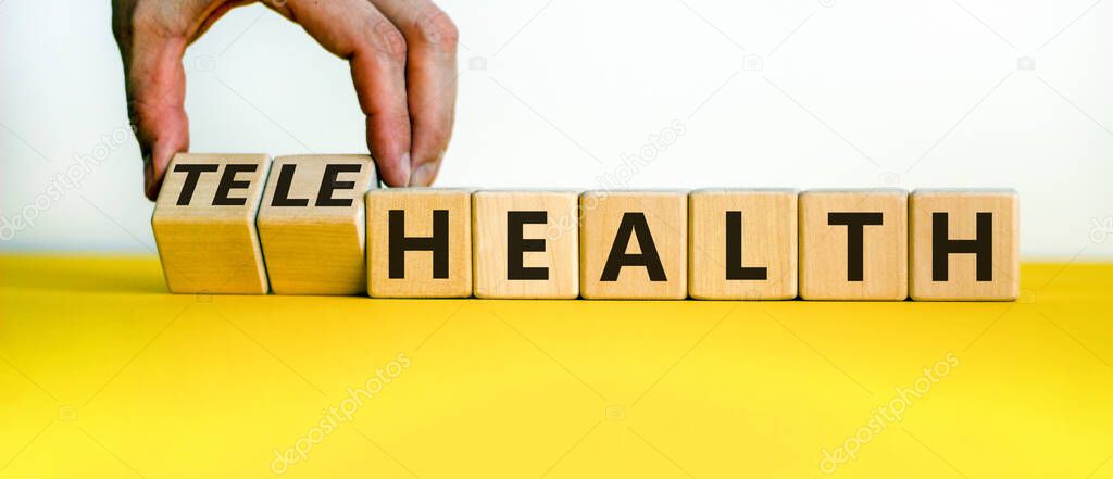 Time to telehealth. Male hand flips wooden cubes and changes the word 'health' to 'telehealth'. Beautiful yellow table, white background, copy space. Business and telehealth concept.