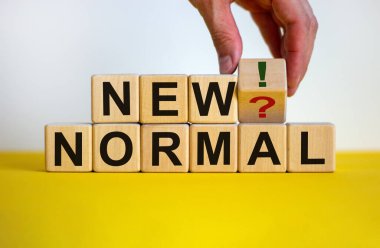 Yeni normale dönme zamanı. Erkek el, soru işareti ve ünlem işareti olan bir küpü döndürür. Kelimeler 'yeni normal'. Covid-19 salgın sonrası konsepti. Güzel sarı masa, beyaz arkaplan, kopyalama alanı.