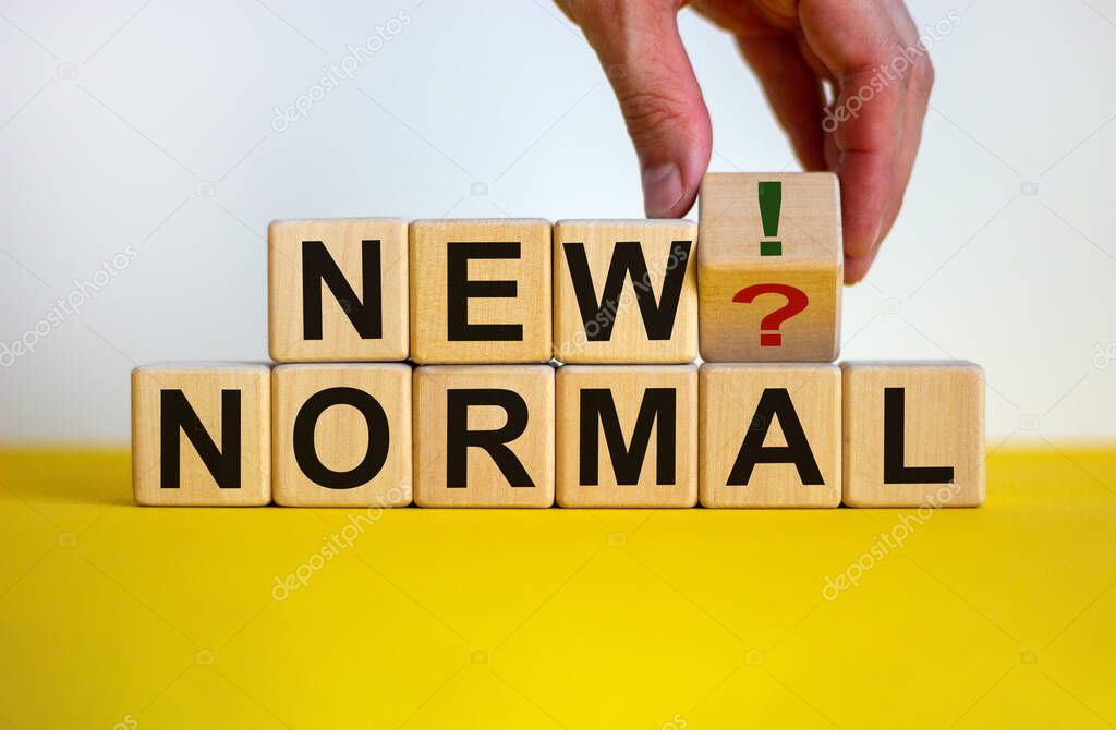 Time to new normal. Male hand turns a cube with question mark and exclamation mark. Words 'new normal'. Covid-19 postpandemic concept. Beautiful yellow table, white background, copy space.