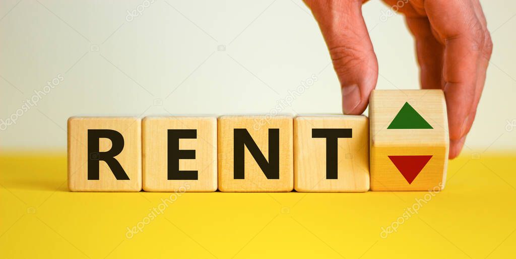 Male hand flips a wooden cube and changes the inscription 'rent up' to 'rent down'. Beautiful yellow table, white background. Business, interest rate, stocks, financial, ranking, mortgage rates concept.