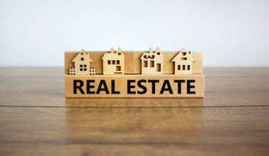 Tahta bloklar 'emlak', minyatür ev, ahşap masa kelimelerini oluşturur. Güzel beyaz arka plan, kopyalama alanı. İş ve emlak kavramı.