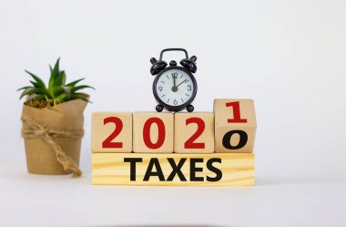 İş ve yeni yıl vergi planlama kavramı 2021. Tahta küpü çevirdim ve 'Vergi 2020' yi 'Vergi 2021' olarak değiştirdim. Siyah çalar saat ve ev bitkisi. Güzel beyaz arkaplan, kopyalama alanı.