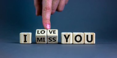 I love you symbol. Hand turns cubes and changes the expression 'I miss you' to 'I love you'. Beautiful grey background, copy space. Psychological and i love you concept.